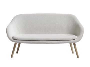 Das About A Lounge Sofa (wollweiß) ist ein modernes hellgraues Sofa mit Holzbeinen, inspiriert von dänischen Design-Sofatrends, dargestellt vor einem weißen Hintergrund.
