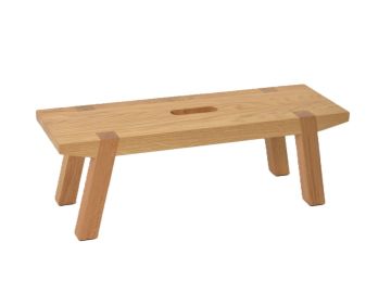 Die Mainzer Fußbank XL ist ein großer Holzhocker mit vier angewinkelten Beinen und einem zentralen Griffschlitz, der aus nachhaltigen Materialien hergestellt wird.