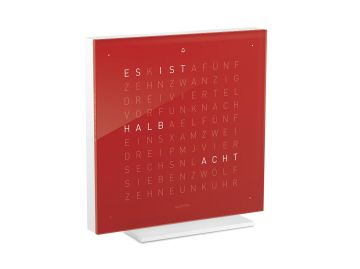 Eine QLOCKTWO EARTH 13.5 PURE (DE) (Kirschkuchen) Tischuhr auf einem weißen Ständer zeigt die Uhrzeit in Leuchtbuchstaben mit der Aufschrift HALB ACHT an.