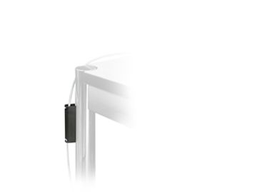 Nahaufnahme einer metallischen Tischecke, an der der USM Haller Magnet-Kabelhalter befestigt ist, der ein weißes, über die Kante geschlungenes Kabel für ein ordentliches Kabelmanagement ordnet.