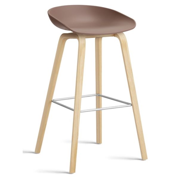 Der About A Hocker AAS32 inkl.. Filzgleiter (Sitzhöhe: 74 cm) aus weichem Ziegelstein verfügt über eine moderne geschwungene Sitzfläche, helle Holzbeine und eine Fußstütze aus Metall, inspiriert von minimalistischen Barhockern, auf weißem Hintergrund.
