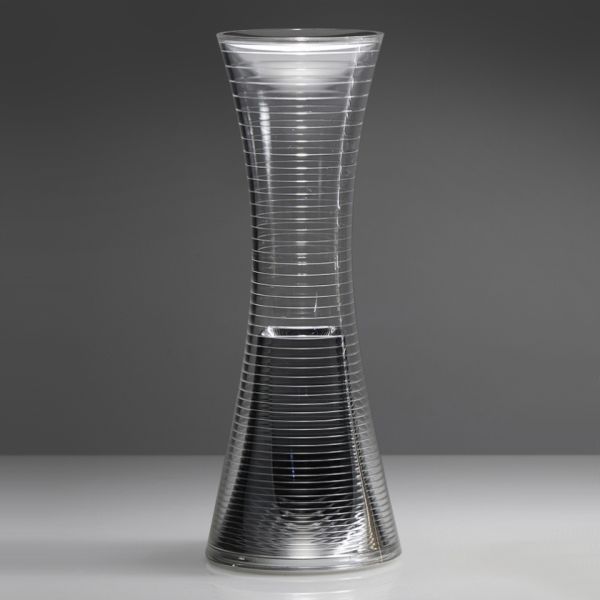 Eine hohe, klare Glasvase in Form einer Sanduhr mit horizontalen Rillen steht vor einem grauen Hintergrund - ihre elegante Form erinnert an die Come together (Aluminium) von Artemide.