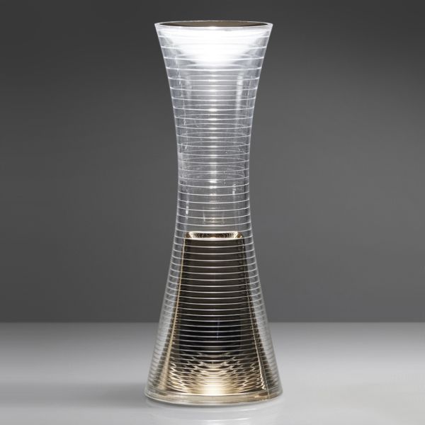 Eine hohe, sanduhrförmige Glasvase mit weißen Streifen und einem dunklen Sockel auf grauem Grund erinnert an das schlichte Design der Come together Kupfer.