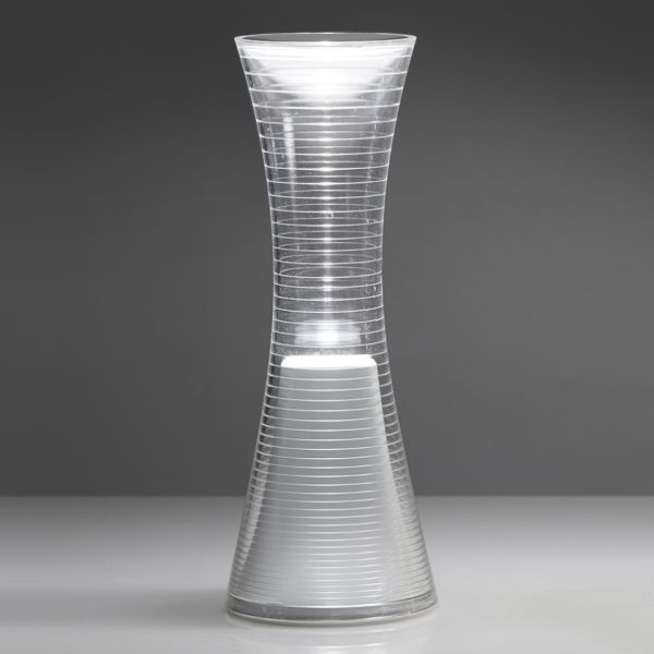 Die Vase "Come together" ist ein modernes, sanduhrförmiges Stück aus klarem Glas mit horizontalen Rillen, inspiriert vom eleganten Stil von Artemide, auf grauem Hintergrund.