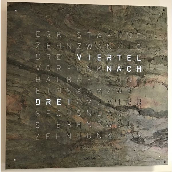 Die QLOCKTWO EARTH 90 (Glintscape) zeigt die Uhrzeit als Worte: VIERTEL NACH DREI in leuchtend weißen Buchstaben auf einem eleganten Stein-Hintergrund.
