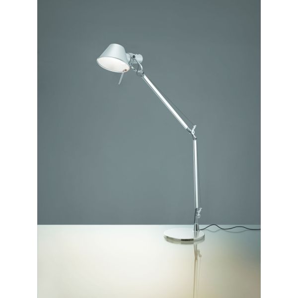 Tolomeo LED verstellbare Schreibtischlampe in Silber, beleuchtet auf einer glänzend weißen Oberfläche mit einem schlichten grauen Hintergrund.